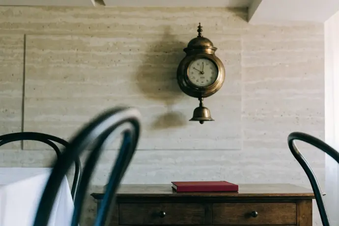 A brass barometer on a pale stone wall above a sideboard with a crimson notebook