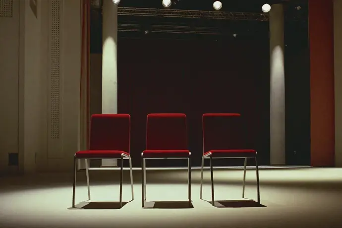 Three empty chairs in a row on a lit conference stage before an event