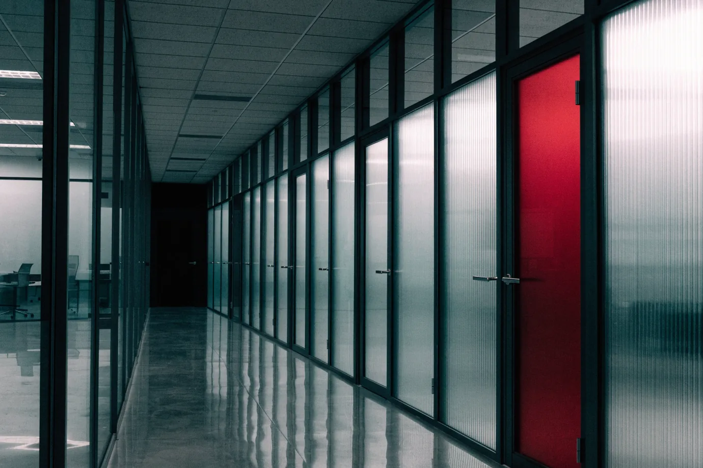 A glass-walled office corridor with frosted doors, one painted crimson