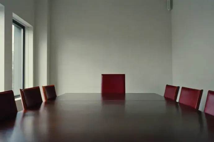 Empty boardroom with a bare table, crimson chairs and grey morning light