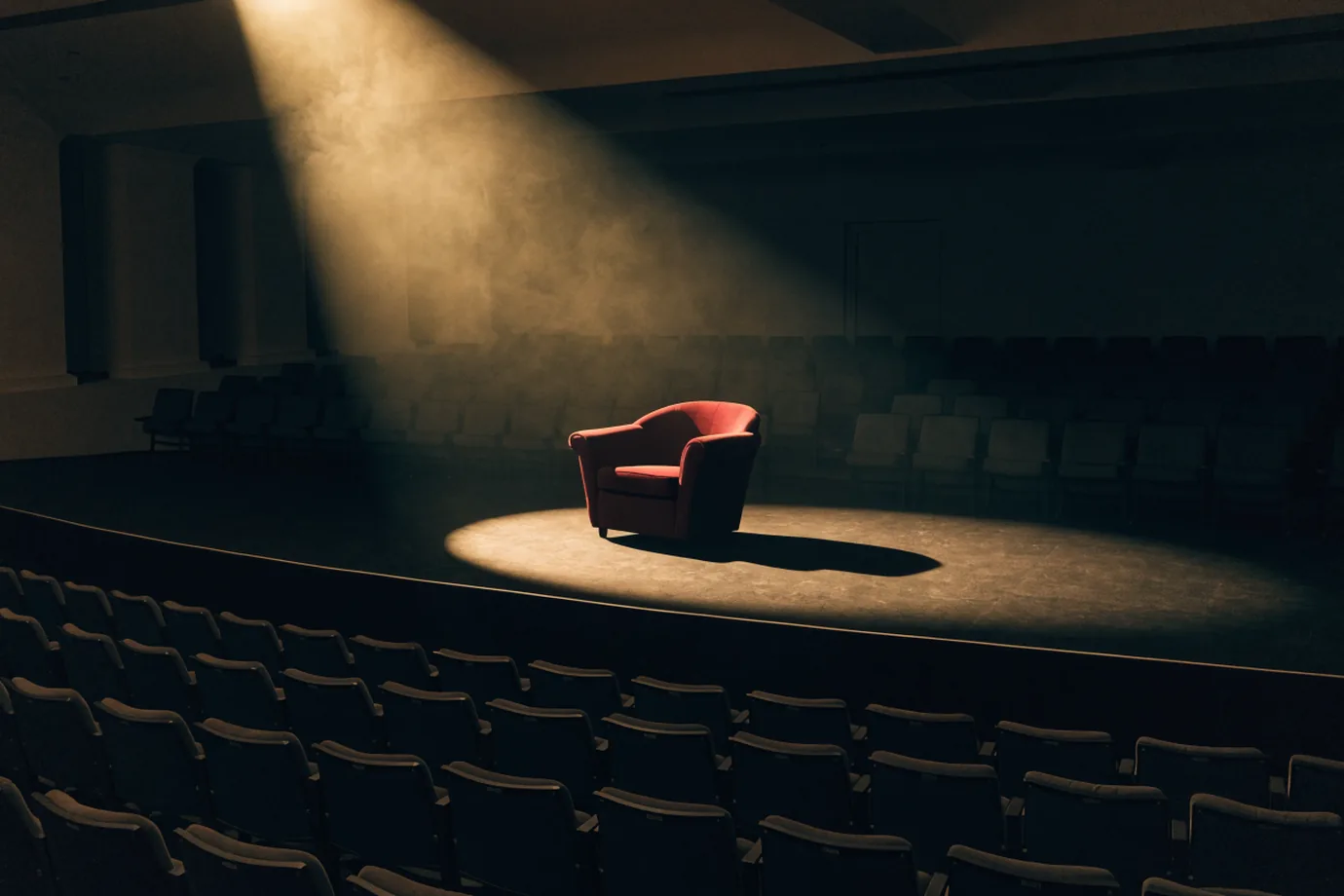 An empty conference stage under a spotlight with a crimson armchair