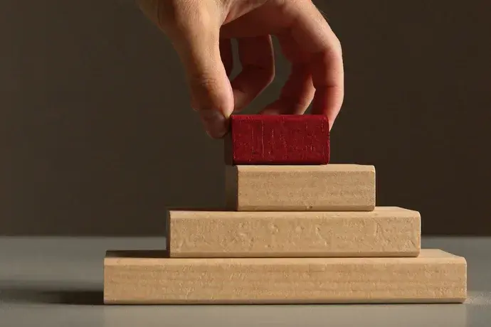 A hand placing the final block on an ascending staircase of wooden blocks