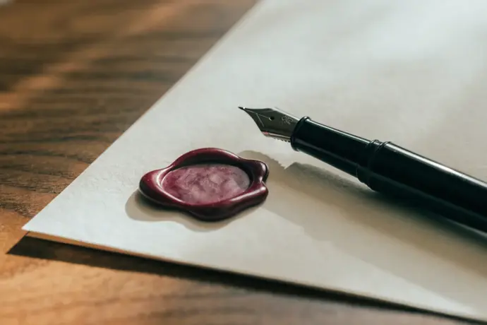 A fountain pen beside a crimson wax seal on cream paper