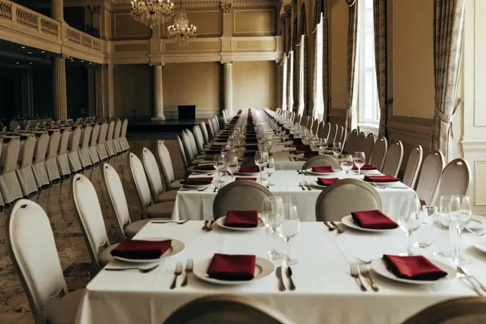 A hotel ballroom set for a gala dinner with white tablecloths and crimson napkins before guests arrive