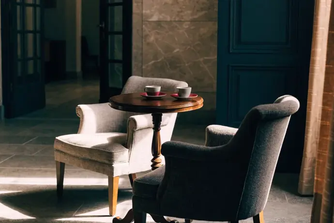 A hotel lobby corner with two armchairs and coffee cups, one on a crimson saucer
