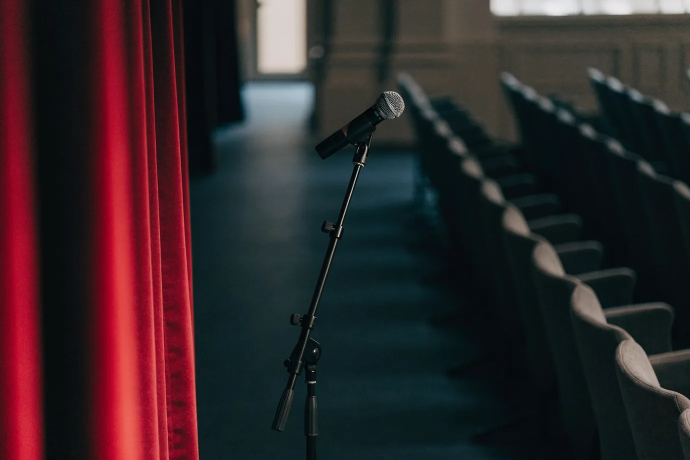 A conference stage seen from the wings with a microphone stand and a crimson curtain