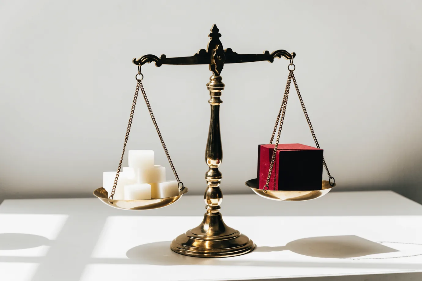 A brass balance scale with white blocks on one side and a single crimson block on the other