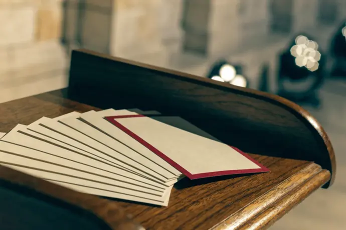 Blank cream cue cards fanned on a wooden lectern, one edged in crimson