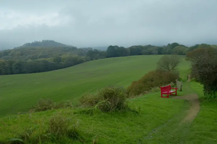 A footpath across green English hills with a crimson red bench beside it