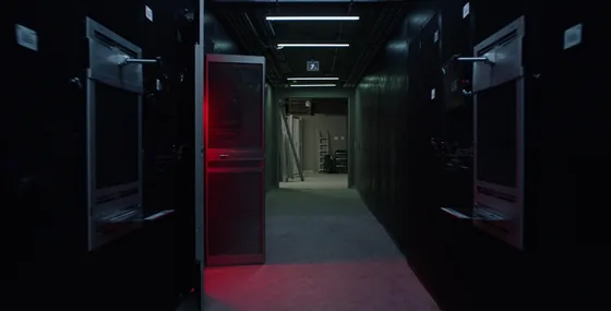 A server room corridor with one rack door open and a crimson red light