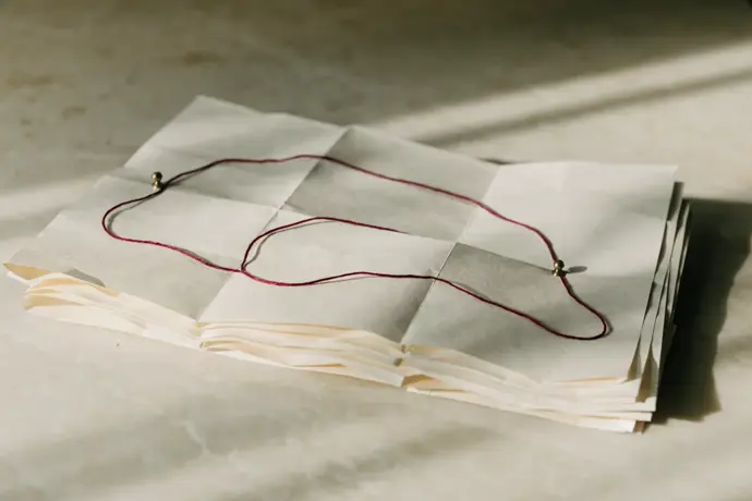 Folded blank maps on a desk with a crimson thread marking a winding route